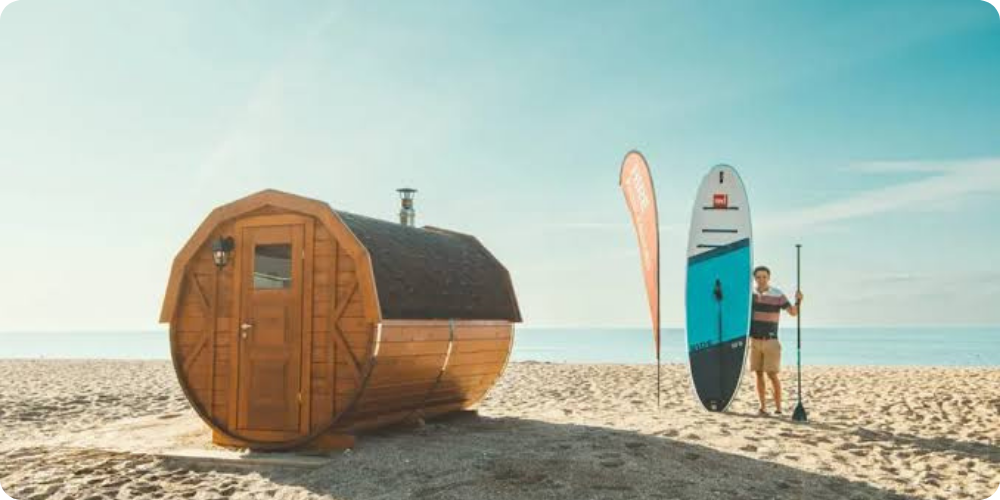 Wood-fired barrel sauna beside a paddleboard on the beach