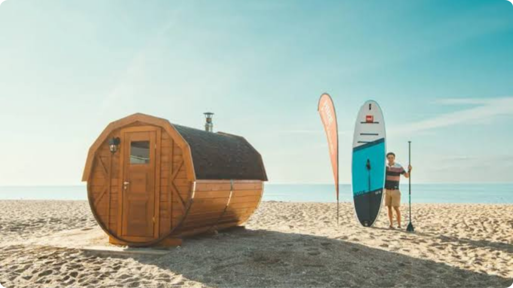 Wooden beach sauna beside a paddleboarder on the sand
