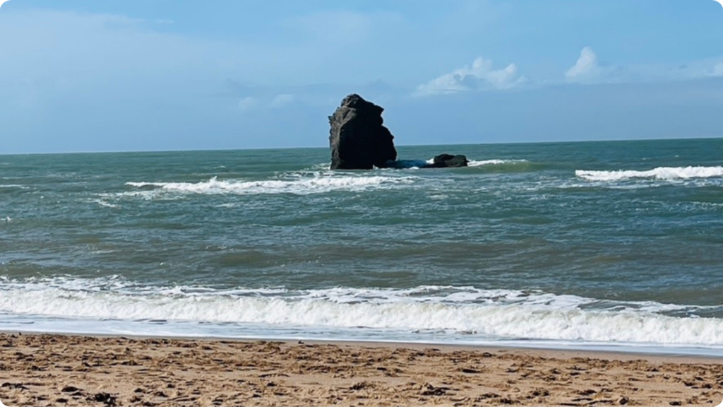 Thurlestone Rock beyond waves breaking on the beach